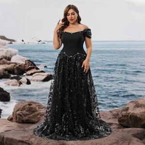 A model wearing a sparkling sequin dress with a flowing skirt, standing on a rocky beach. A stunning choice for a wedding guest dress.